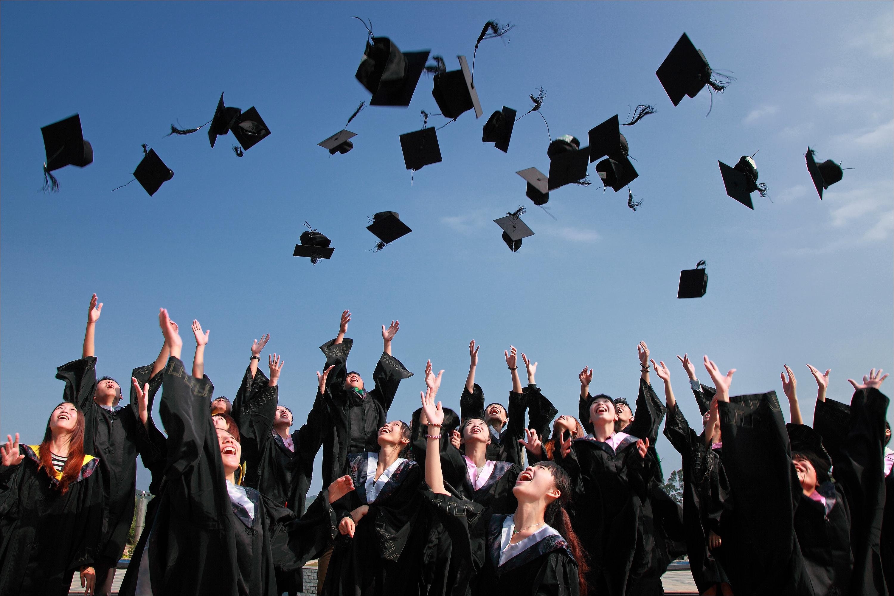 Graduation hats thrown in air by people