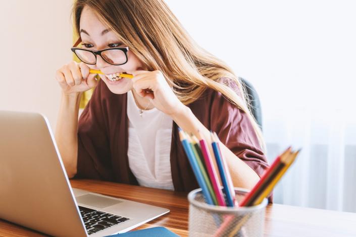 Woman looking at laptop with pencil in mouth learning