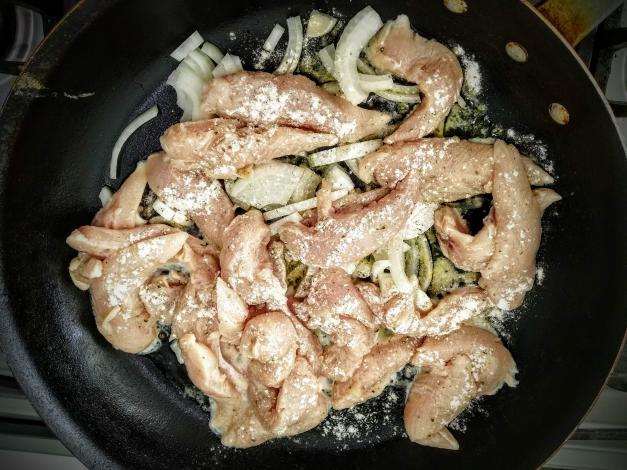 Chicken and onions in frying pan cooking
