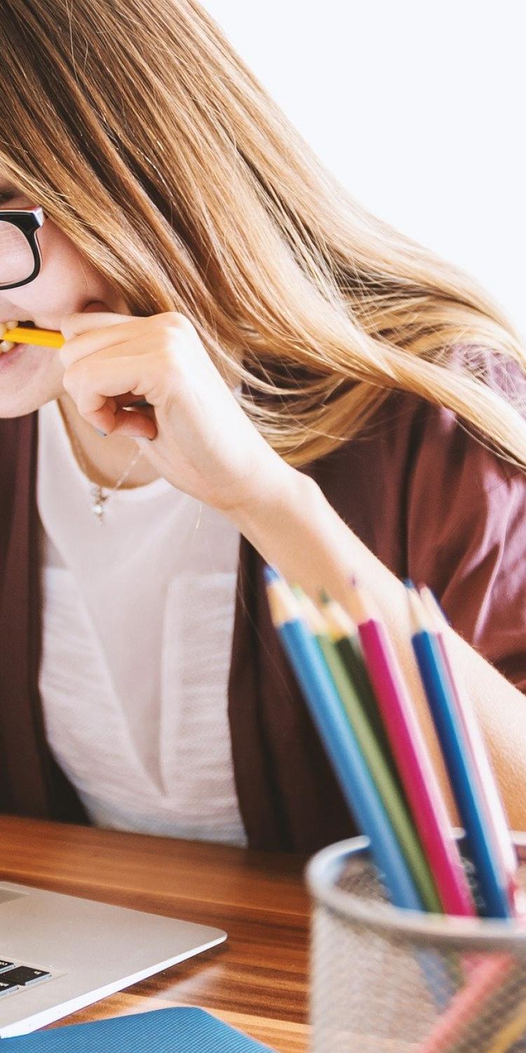 Woman looking at laptop with pencil in mouth learning