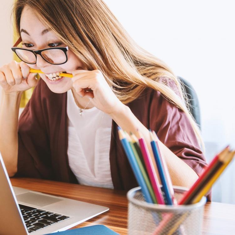 Woman looking at laptop with pencil in mouth learning